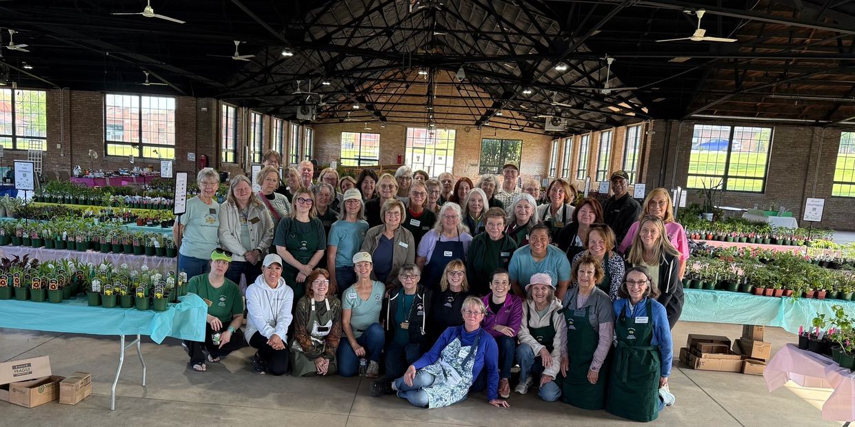 Group of people posing in a large indoor market with plants and flowers.
