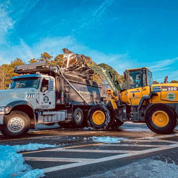 A yellow Komatsu loader fills a dump truck with snow on a sunny day.