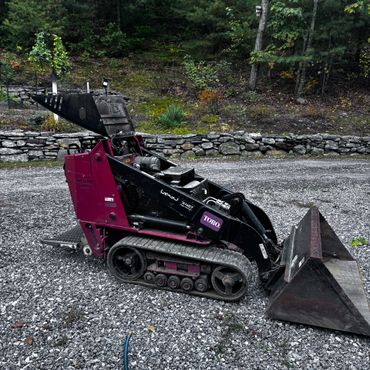 Compact Toro mini skid steer loader on gravel driveway near stone wall.