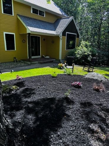 Yellow house with a freshly mulched garden bed and rocking chairs on the lawn.