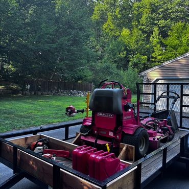 A red Gravely lawn mower and equipment on a trailer in a green backyard.
