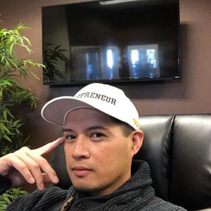 Man wearing a white cap and dark sweater sitting indoors.