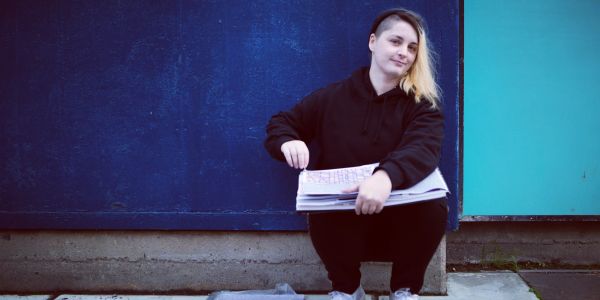 Person sitting and holding papers against a wall.