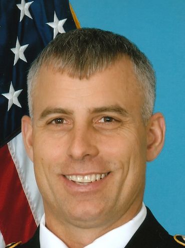 Portrait of a smiling military officer with an American flag background.