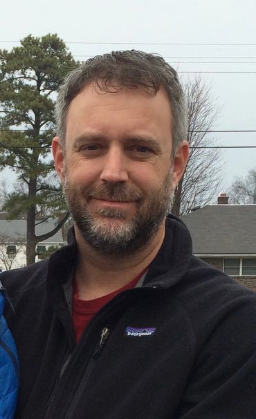 Smiling man with beard wearing a black Patagonia jacket outdoors.
