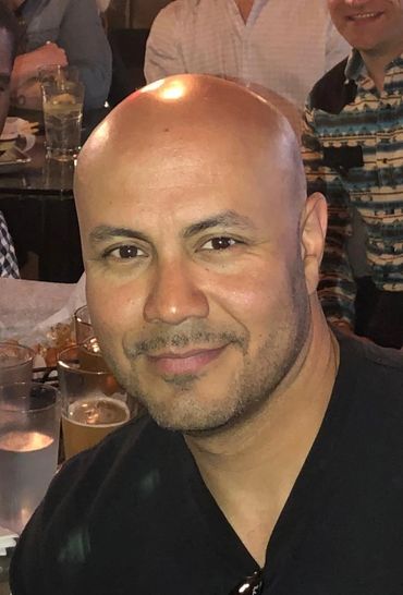 Smiling bald man in a casual setting with drinks in the background.