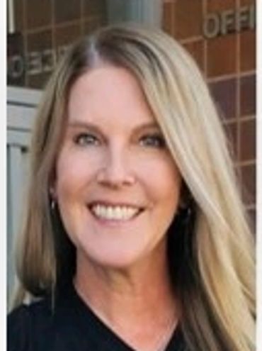 Smiling woman with long blonde hair outdoors in front of a brick wall.