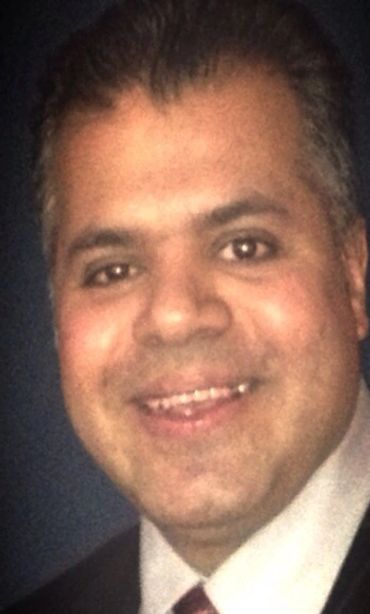Close-up portrait of a smiling man in formal attire against a dark background.
