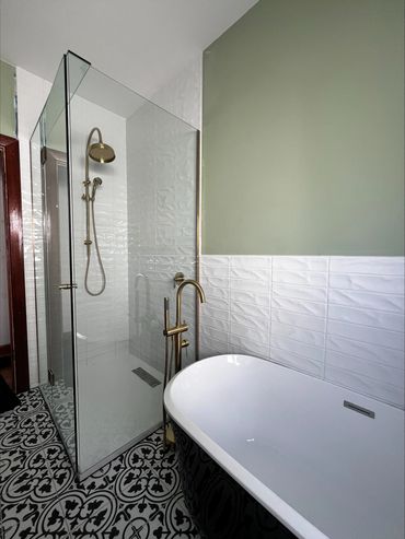 Modern bathroom with glass shower, black bathtub, and patterned floor tiles.