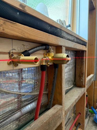 Laser level tool aligns plumbing pipes on a wooden wall frame.