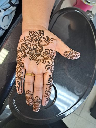 Intricate henna design on a hand with a gold ring.