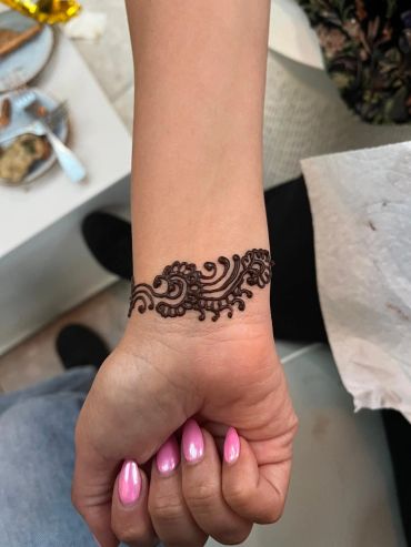 Intricate henna bracelet design on wrist with polished pink nails.