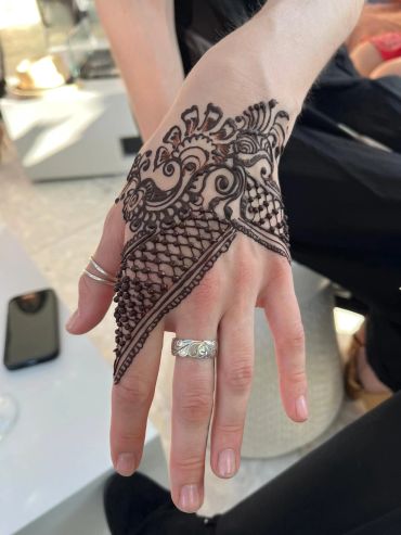 Intricate henna design on hand with silver rings.