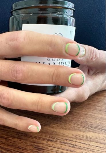 Hand with nails featuring green and white French tip manicure holding a black jar.