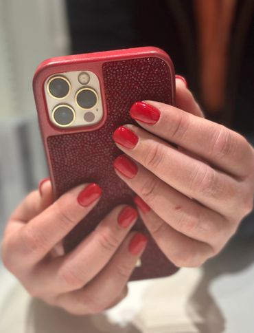 Hands with red nail polish holding a red phone case with triple camera lenses.