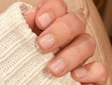 Manicured nails with subtle gold glitter near cuticles on a cozy white knit sleeve.