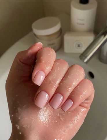 Hand with soft pink polished nails, covered in water droplets.