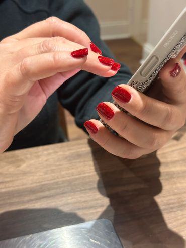 Hands with glittery red nail polish holding a phone with a Swarovski case.