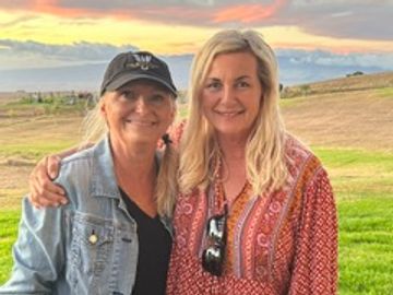 Two women smiling outdoors at sunset.