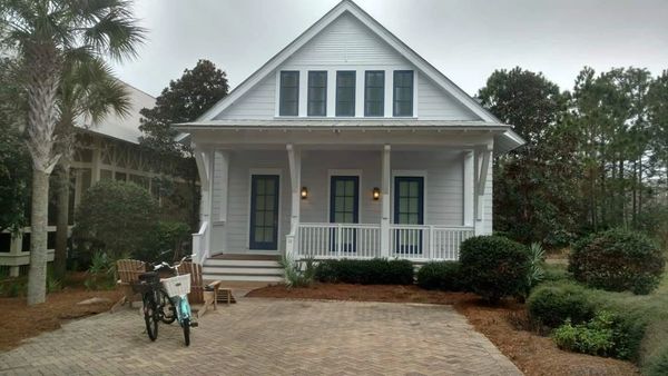 Cozy white house with blue doors, porch, and two bicycles parked outside.
