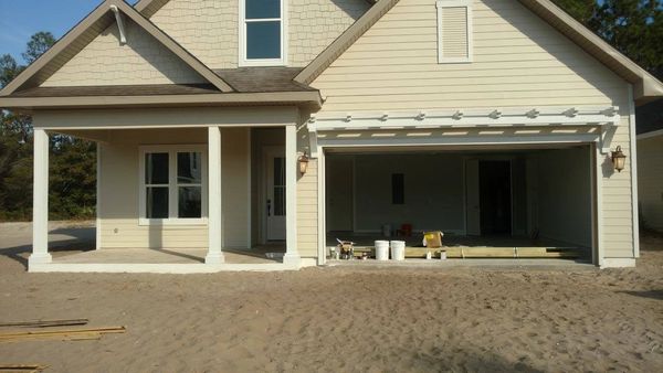 Newly constructed beige house with open garage and sandy yard.