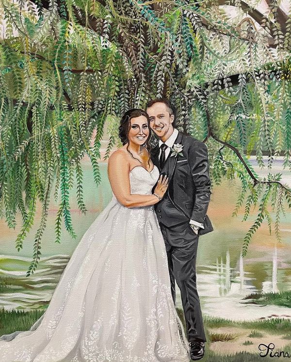 A bride and groom pose happily under lush green foliage by a serene lake.
