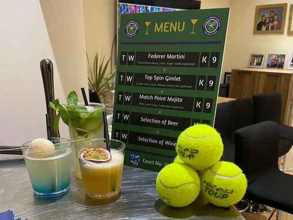 Cocktails and tennis balls on a metallic table with a drink menu in the background.