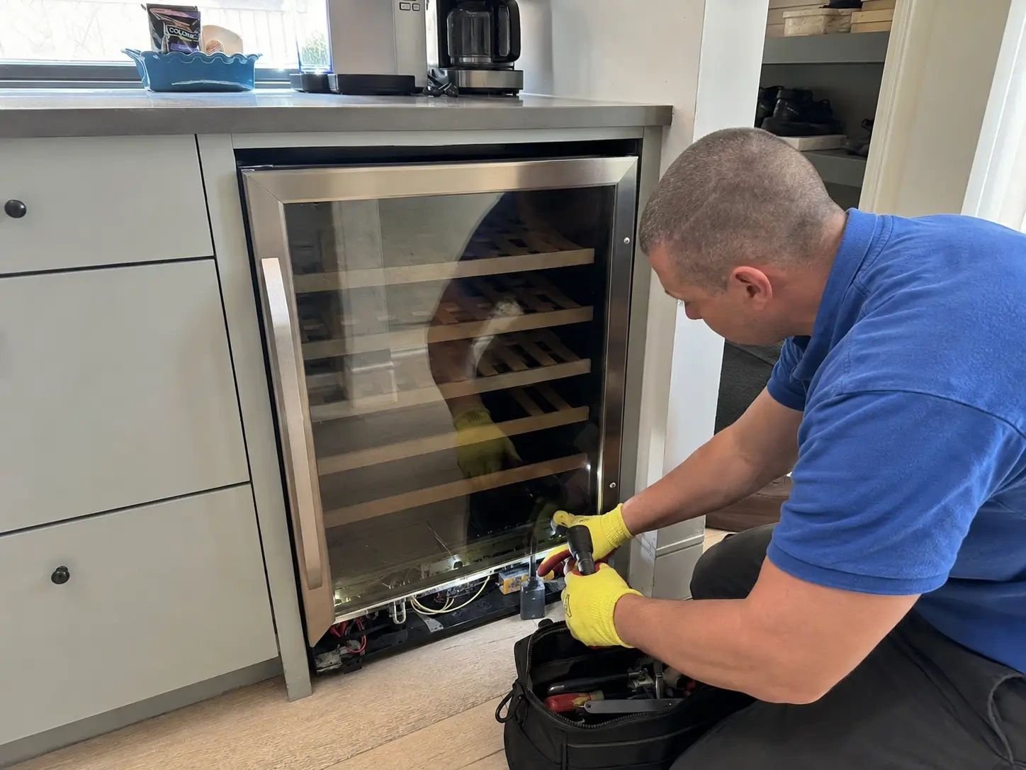 Technician inspecting and servicing a built-in under-counter wine cooler in a residential kitchen in