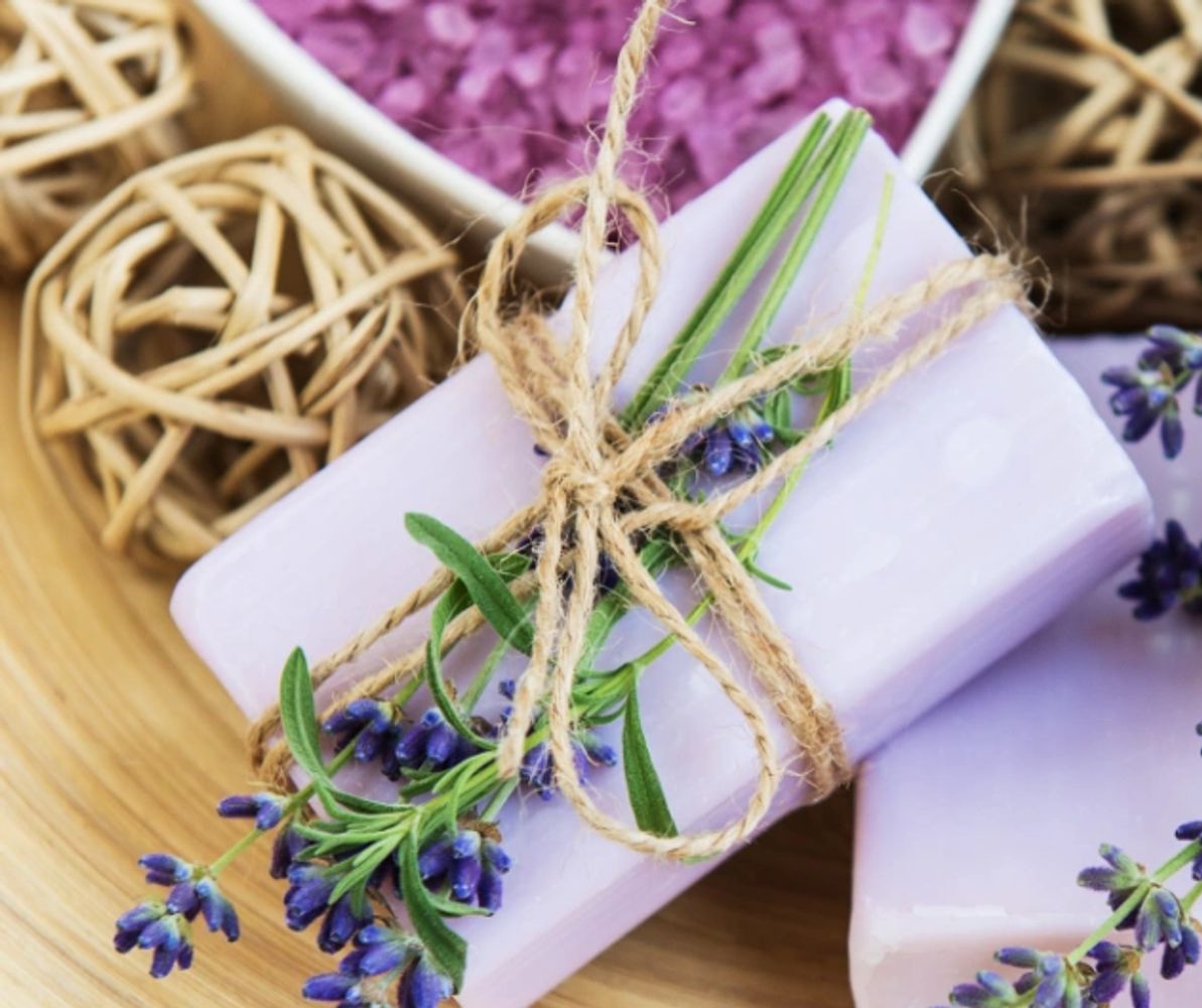 Two purple bars of handmade soap next to container of bath salts.  One is wrapped in twine.