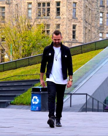Man walking outdoors near a recycling bin with a historic building in the background.