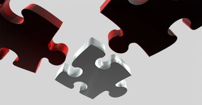 Close-up of puzzle pieces with one silver piece fitting in between black pieces.