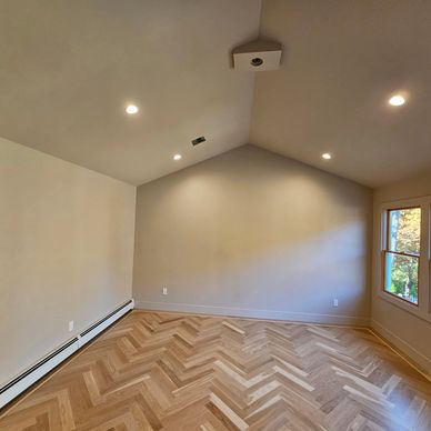 Empty room with herringbone wooden floor and large windows.