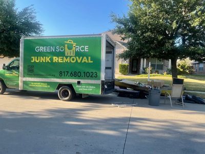 Green Source Junk Removal truck parked with junk and furniture outside a house.