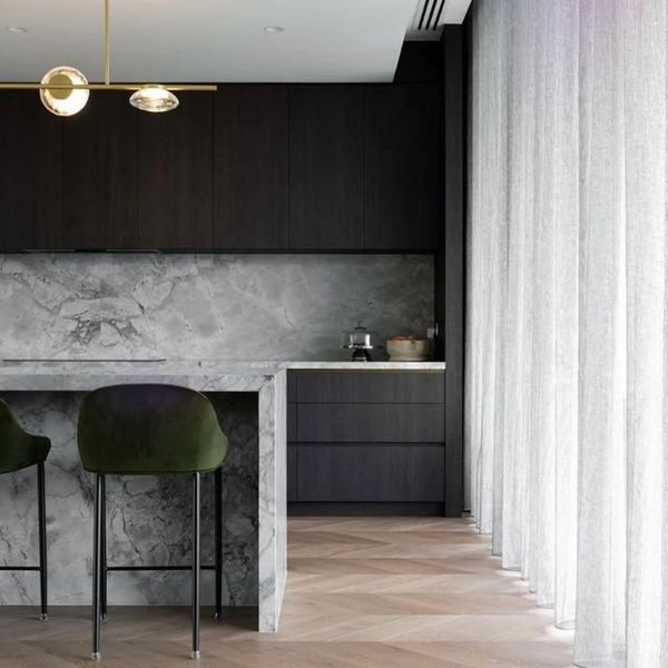 Modern kitchen with marble island, dark cabinets, and large sheer curtains.