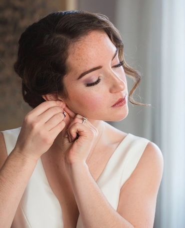 Woman in white dress putting on earrings, preparing for an event.