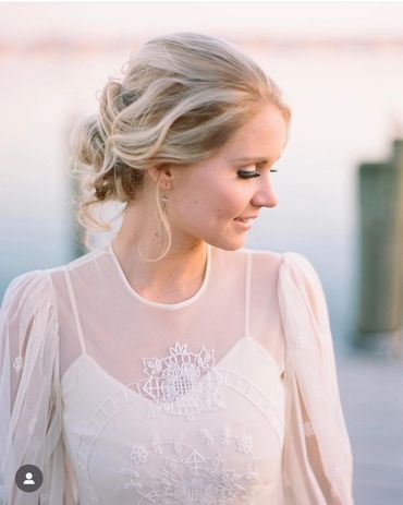 A bride in a delicate white dress with intricate lace details, looking down with a serene smile.
