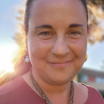 Woman smiling outdoors with sunlight behind her.