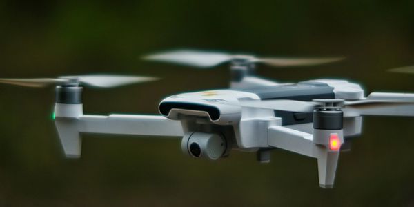 A white drone flying with spinning propellers in a blurred green background.