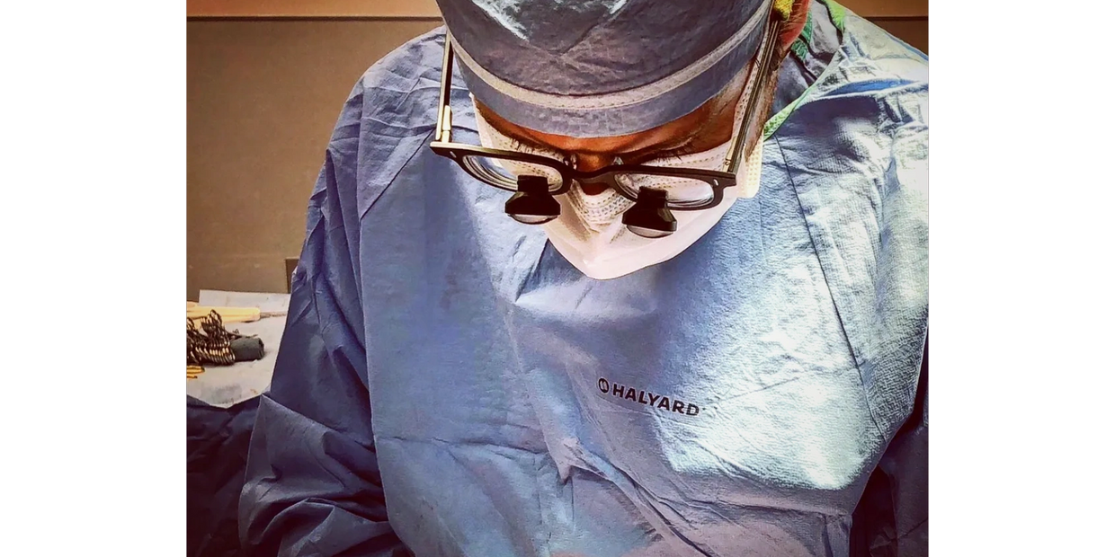 Photo of Dr. Chupp operating with surgical loupes, a surgical mask, gown, and surgical cap (PPE)