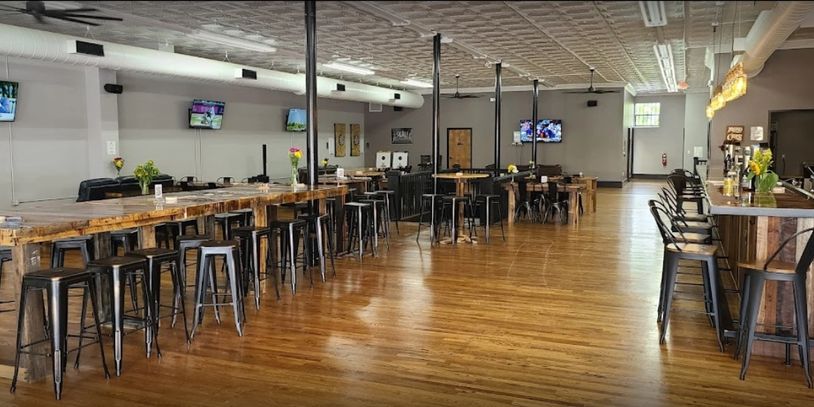 Spacious bar with wooden floors, high stools, and multiple TV screens.