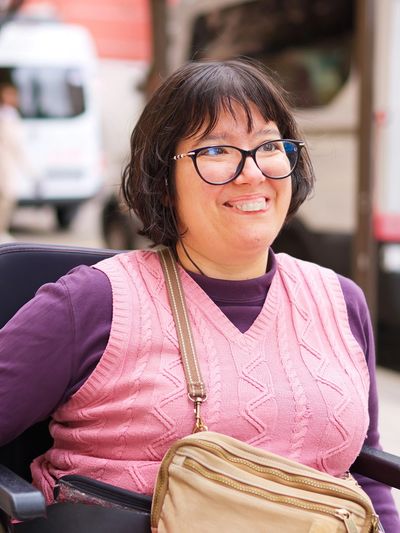 Woman with glasses wearing a pink sweater vest and smiling outdoors.