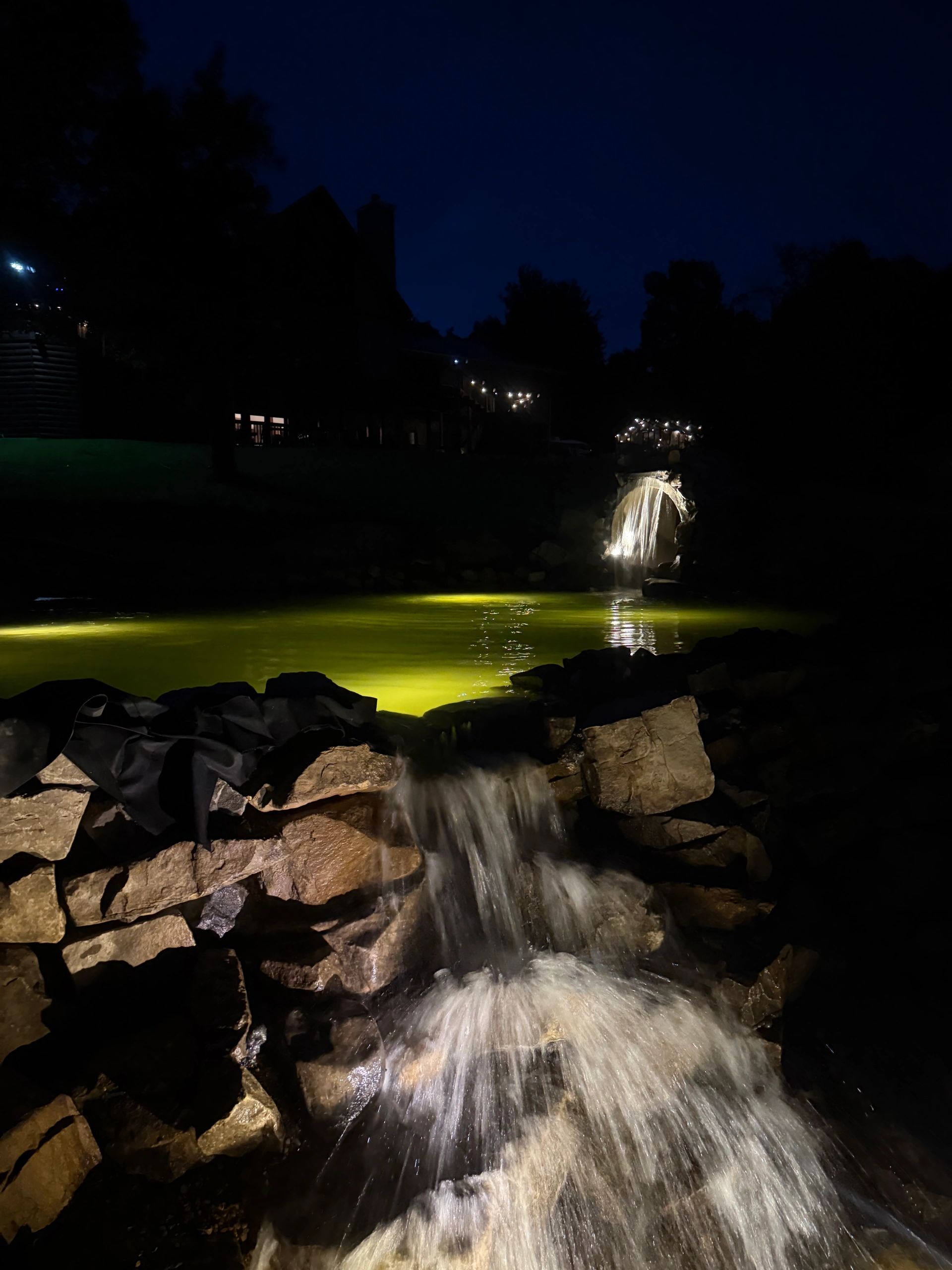 Waterfall cascading over rocks at night with illuminated pond.