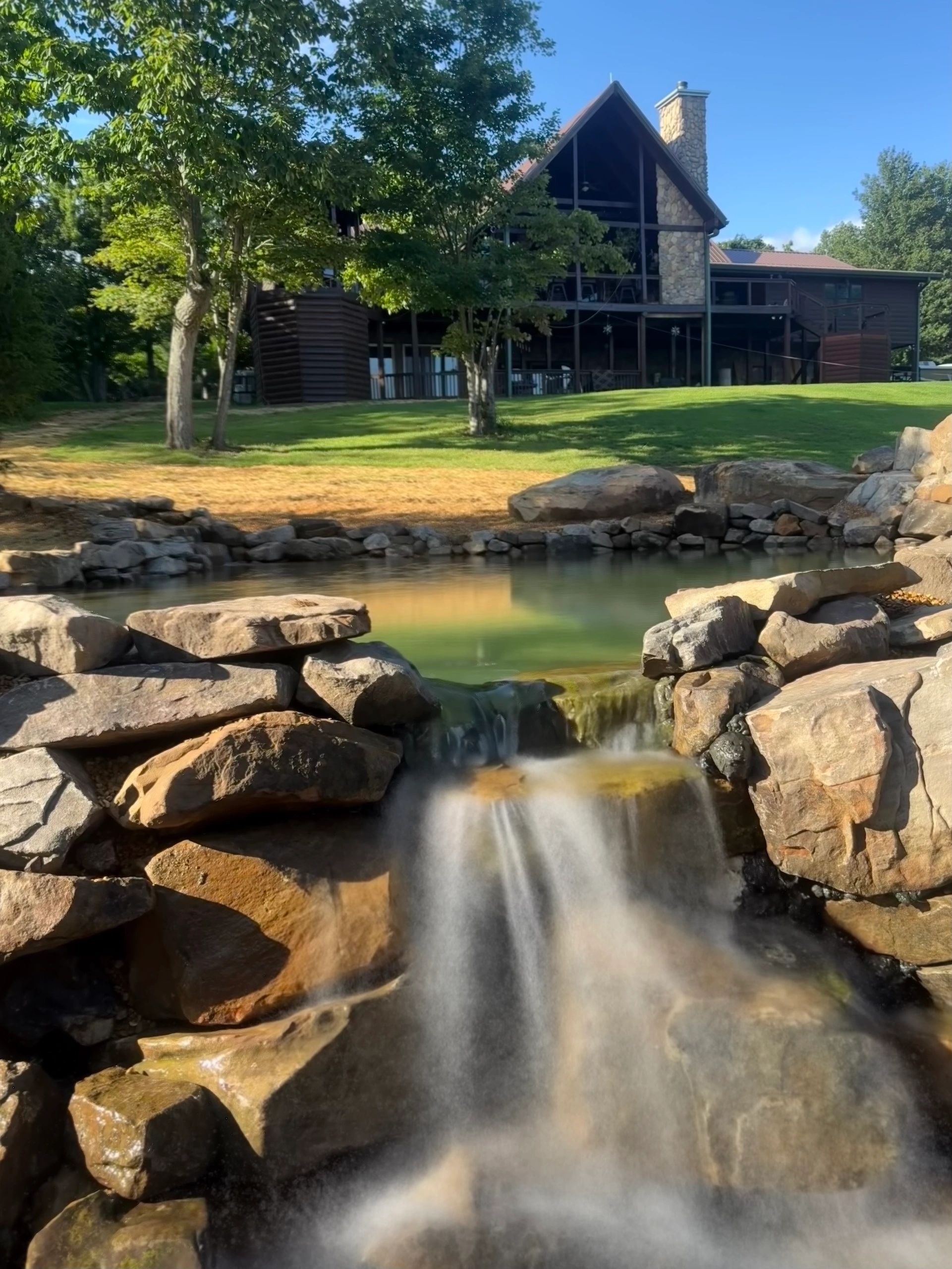 Waterfall in front of a cabin by a pond.