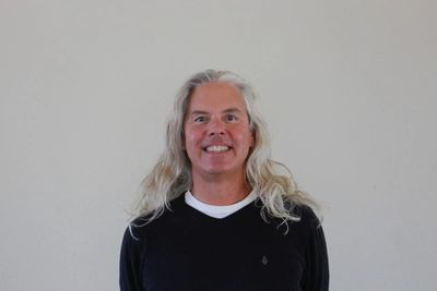 Smiling man with long gray hair wearing a black sweater.