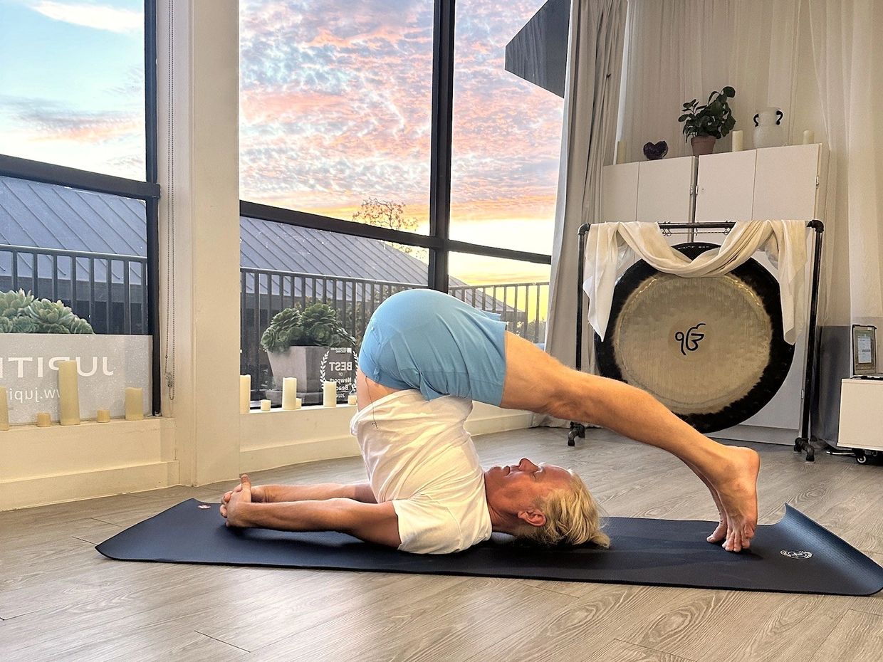Juris Zinbergs in Plow pose in a yoga studio at sunset