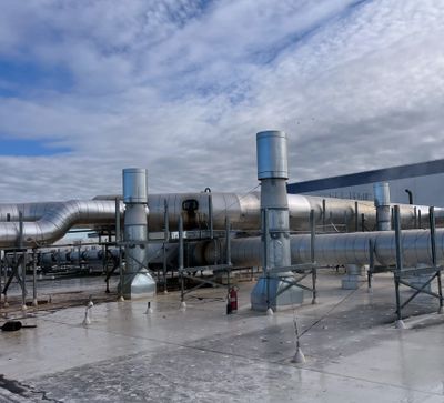 Industrial rooftop with large silver ventilation pipes under a cloudy sky.