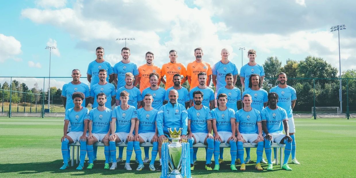 Manchester City football team posing with the Premier League trophy outdoors.