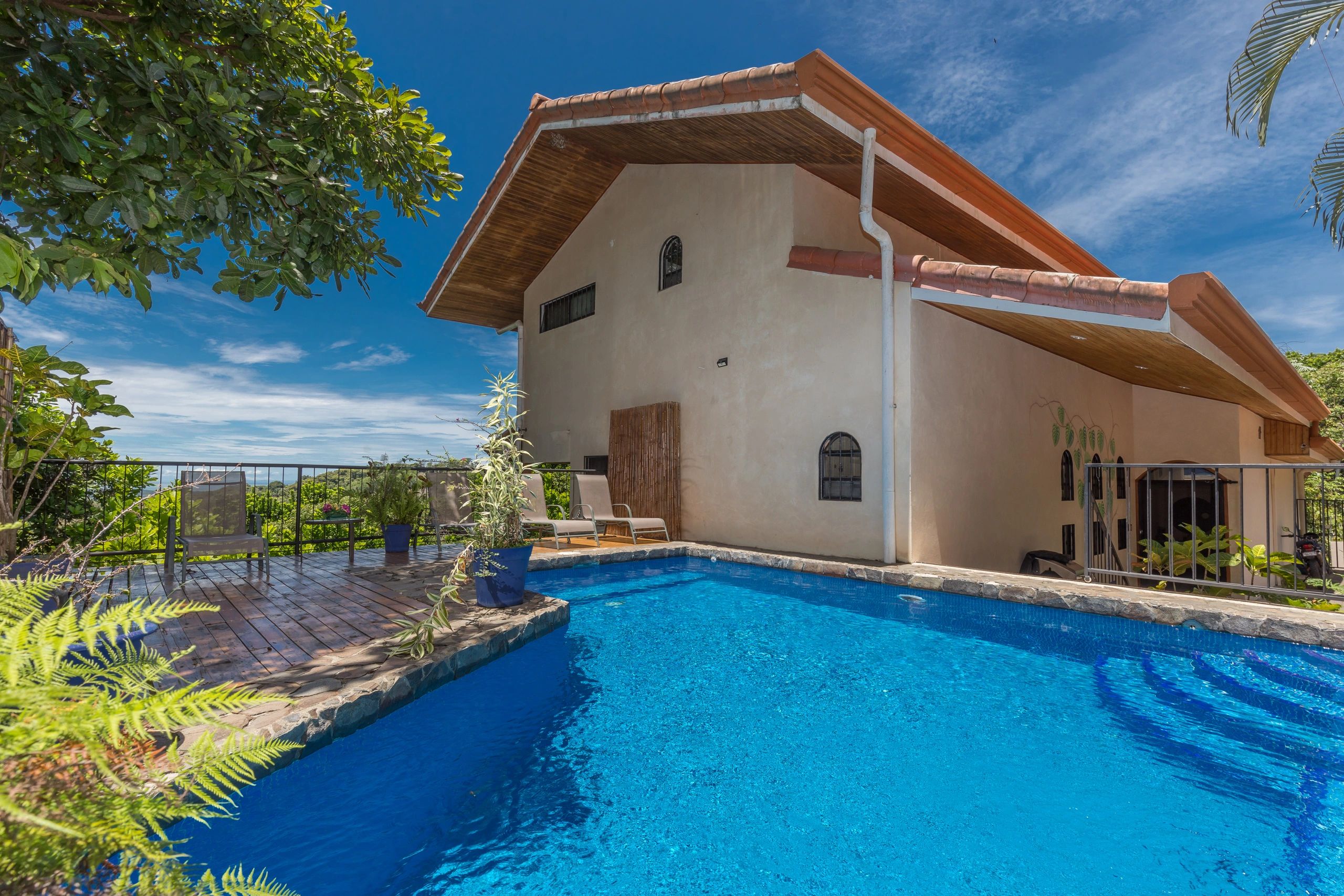 A serene backyard with a swimming pool and lounging area beside a house under a clear blue sky.