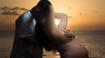 A beautiful brown pregnant woman in the ocean with her head cradled by her lover.