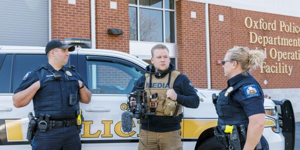 Police officers and a media person talking outside a police department building.
